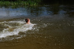 Child dives into the river with a running start. The boy jumps, swims and splashes in the river in the summer time