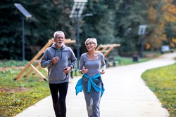 Aged couple jogging in the public park and smile