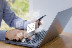 Digital newsletter and Email marketing concept. Hand of Businessman working on Laptop and mobile smartphone with email icon for the company sending many e-mails or digital newsletter to customers.