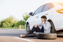 Asian young man using smartphone called a car repair shop or someone close to help after trying failed to fix a problem on the road, Car broke down or changing flat tire on the road concept.