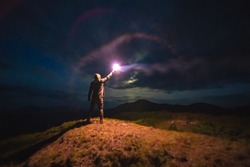 The man with a bright firework stick standing on a mountain. evening night time