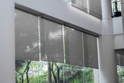 Close up luxury Long blind, curtain, roller, shade, shutter protected sunlight with large glass wall and blur green tree background.