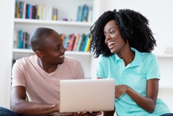 Laughing african american couple with computer indoors at home