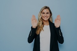 Portrait of young woman refusing offer in polite manner smiling friendly with positive look as waving hands in stop gesture being not interested isolated over blue studio background with copy space