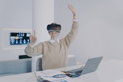 Young european woman in VR headset in office. Student of futuristic college. Girl working on project in cyberspace. Concept of being in virtual reality and simulation in education.