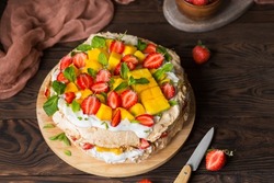 Pavlova with strawberries, mango and coconut cream. Cakes made of cane sugar. Tropical cake. Exotic dessert with mint. Strawberries on a wooden table. New Zealand food