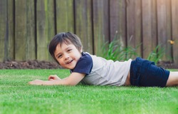 Active kid having fun lying down on green  grass in the garden. Healthy Child boy laying on lawn Relaxation happy childhood enjoying summer day concept