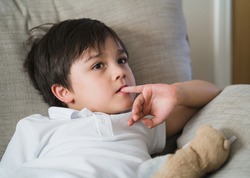 Child putting finger in his mouth.Schoolboy biting his finger nails while watching TV, Emotional kid portrait, Young boy siting on sofa looking out with thinking face or nervous, Children Health care 