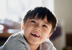 Close up happy kid looking up with smiling face, High key light healthy child relaxing at home, Positive Little boy having fun on his own in living room with blurry sunny light background.