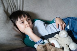 Candid shot of Mixed race kid lying on sofa biting his finger nails while watching TV, Child boy laying on couch and bite his nails, Emotional child portrait, Children Health care concept
