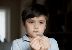  Pottrait School Kid looking out deep in though, Selective focus Child boy holding one pound coin looking out with sad face, Bored Child standing alone in living room, Children learning to save money 