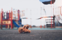 Lost teddy bear toy lying  on playground floor in gloomy day,Lonely and sad brown bear doll lied down alone in the park, Lost toy or Loneliness concept,International missing Children day
