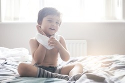 A blurry picture of happy little boy sitting in bed and try to wearing his cloth with smiling,Concept learning at home,  filtered tones , retro color                                