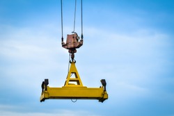 Automatic spreader of an industrial crane hanging in the air with blue sky background