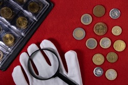 Collection of coins and collector white gloves and magnifying glass on red
