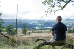 Man Sitting on Branch Looking out at the beautiful view of Ullswater Lake, Lake District, England