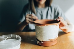 Girl paints a flower pot with white paint, hobby and decorative work