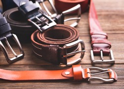 Collection of leather belts on a wooden table. Leather colored belts.