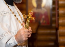 The priest of the Orthodox Church holds a golden cross. A golden cross in the hands of a priest. A male priest holds a large Orthodox cross.
