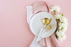 White plate, white gold colors cutlery  and white flowers table place setting  on pink background top view.  Space for text.  Holiday, birthday, wedding invitation template.