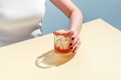 Glass with Whiskey and Ice Cube in Woman Hand on Table on Blue Background. Modern Isometric Style. Creative Concept