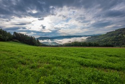 Colorful rural panoramic landscape image with a wide view over fields,forest,hills and foggy valleys towards the horizon and a blue sky with clouds