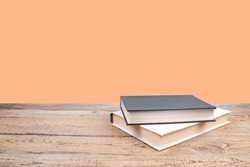 Composition with hardback books, fanned pages on wooden deck table and orange background. Books stacking. Back to school. Copy Space. Education background