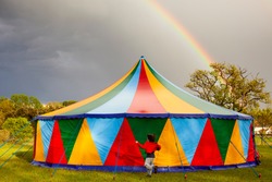 Colored circus tent in a rainy day with a rainbow on the sky