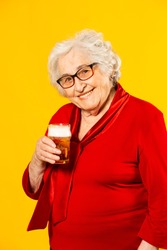 Studio portrait of a senior woman wearing red shirt with a glass of a half pint beer, against a yellow background