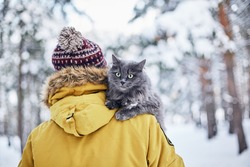 Young man with fluffy cat in winter forest 