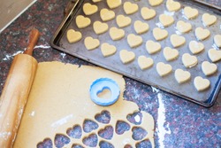 Heart shaped cookies in the making next to a wooden rolling pin, raw dough and heart shaped cookie cutter
