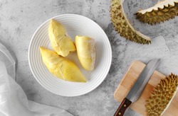 Topview of ripe durian, wood cutting board with knife and durian rind on table.