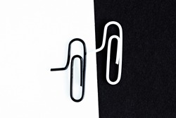 A white-clipped paperclip sits on a black surface and another black paperclip sits on a white surface - black and white concept with paperclips - stark contrasts and differences as background