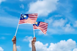 Hand happily waving Malaysia flag against blue sky. Celebrate Independence Day & Merdeka day.