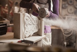 Female sculptor cutting a white marble piece with a power tool, craftswoman shaping a sculpture with an angle grinder, caucasian woman working inside an arts workshop, detail closeup of hands and dust