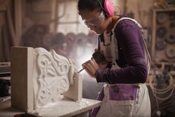 Female sculptor working on a piece using hammer and chisel, sculpting a white marble stone into a beautiful pedestal, stonemasonry and stonecraft