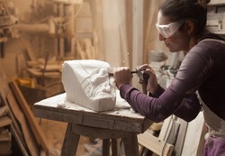 Female sculptor at work in a workshop, using hammer and chisel to sculpt a piece of white marble stone, debris and particles flying around, stonemasonry and stonecraft, copy space