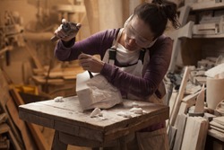 Female sculptor at work in a workshop, using hammer and chisel to sculpt a piece of white marble stone, stonemasonry and stonecraft