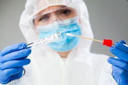 Medical healthcare NHS technician holding COVID-19 swab collection kit,wearing white PPE protective suit mask gloves,test tube for taking OP NP patient specimen sample,PCR DNA testing protocol process