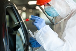 Medical worker in personal protective equipment swabbing a person in a car drive through Coronavirus COVID-19 mobile testing center,oral and nasal specimen collection procedure,health and safety 
