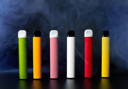 Set of colorful disposable electronic cigarettes on a black background with smoke. The concept of modern smoking, vaping and nicotine.
