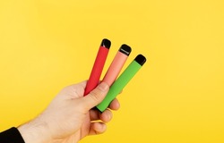 Disposable electronic cigarettes of different flavors in hand on a yellow background. The concept of modern smoking, vaping and nicotine.