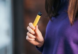 Yellow disposable electronic cigarette in a woman's hand. Modern smoking 