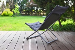 Folding chair surrounded by green leaves on a wooden deck. Relaxation in the garden. Cottage aesthetics. Vacation outside the city. Warm summer day. terrace