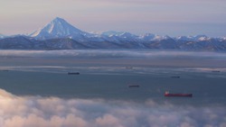 In Kamchatka early in the morning at dawn in the fog ships are in the Pacific ocean on the background of a volcano