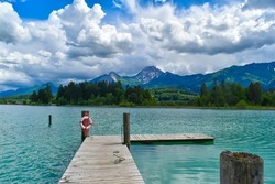 Relaxing mountain view of a dock on a tranquil lake with turquoise water. Cloudy blue sky
