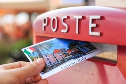 Male send a postcard to a red mailbox in Liguria, Italy. The postcard shows a Liguria coast, Sestri Levante city 