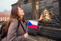 woman wawing with Chezh flag in Charles Bridge and making a wish touching the bronze plaque bridge for good luck