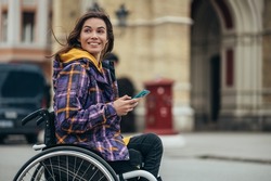 Young beautiful woman with disability who uses a wheelchair using a smartphone while out in the city