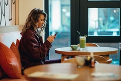 Beautiful young woman drinking matcha latte coffee and using smartphone in a cafe